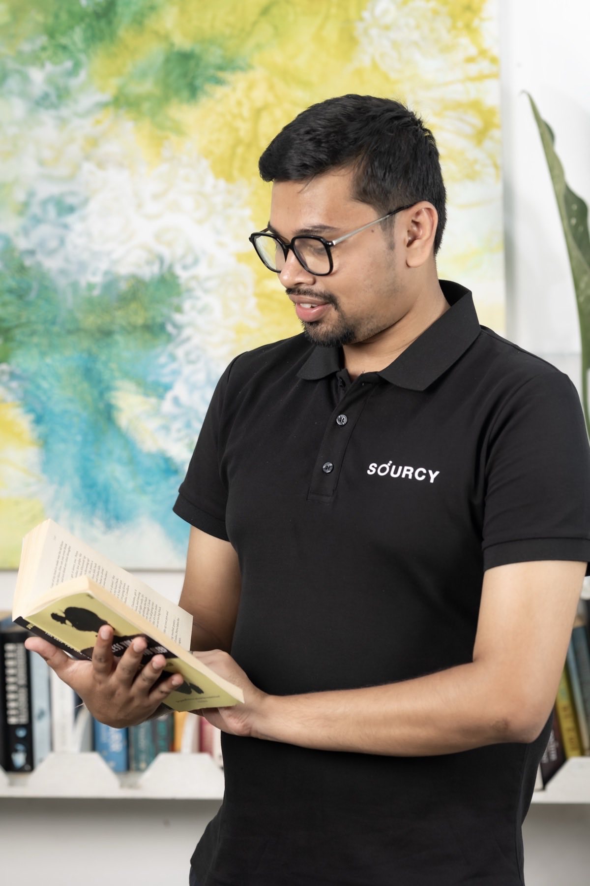Prakhar Varshney reading a book in a studio, wearing a Sourcy polo shirt